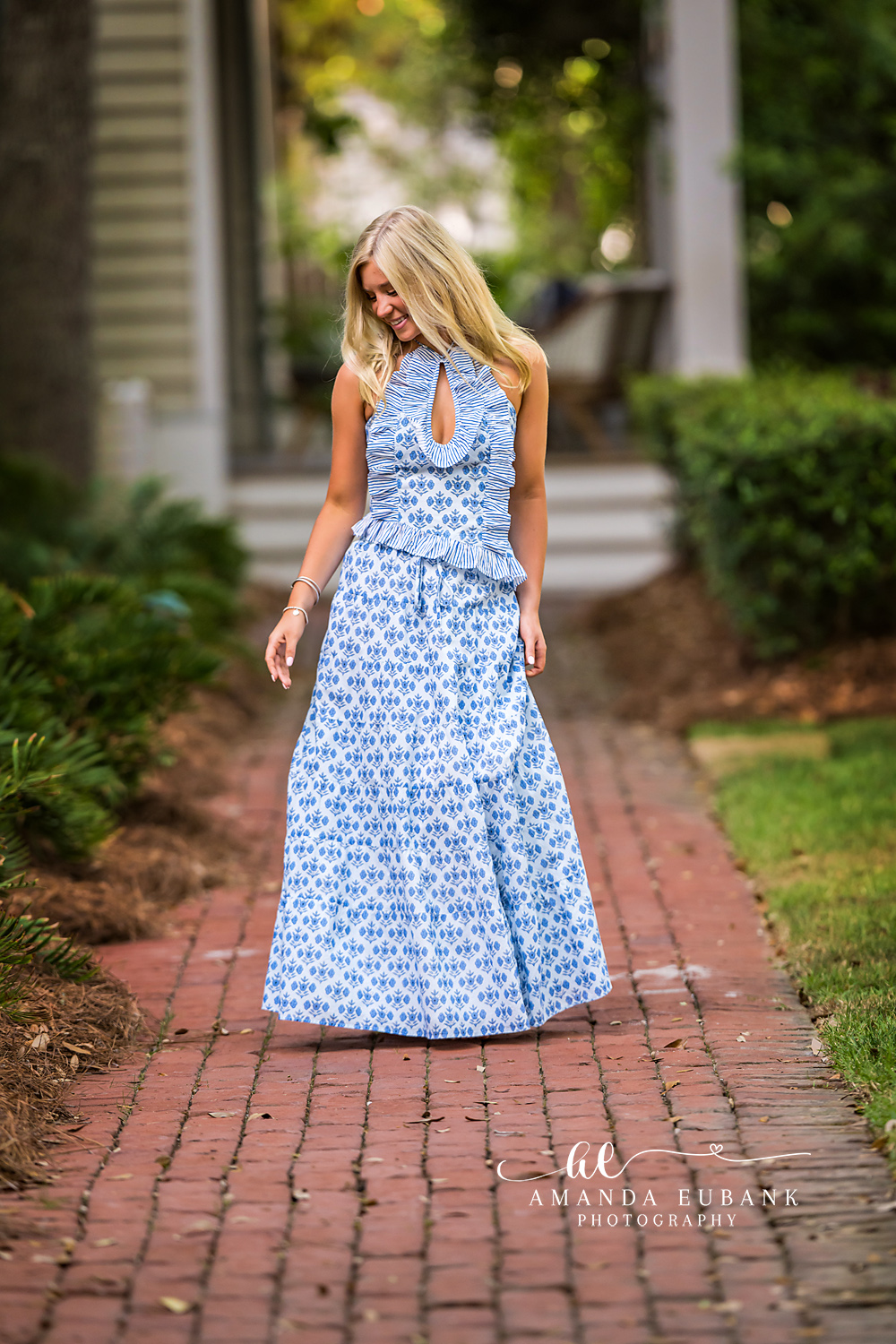 Rosemary Beach Brick Paver Walk Senior Portrait | 30A Senior Photographer Senior girl walking down a Rosemary Beach brick paver street in a blue and white halter maxi dress with hair flowing forward