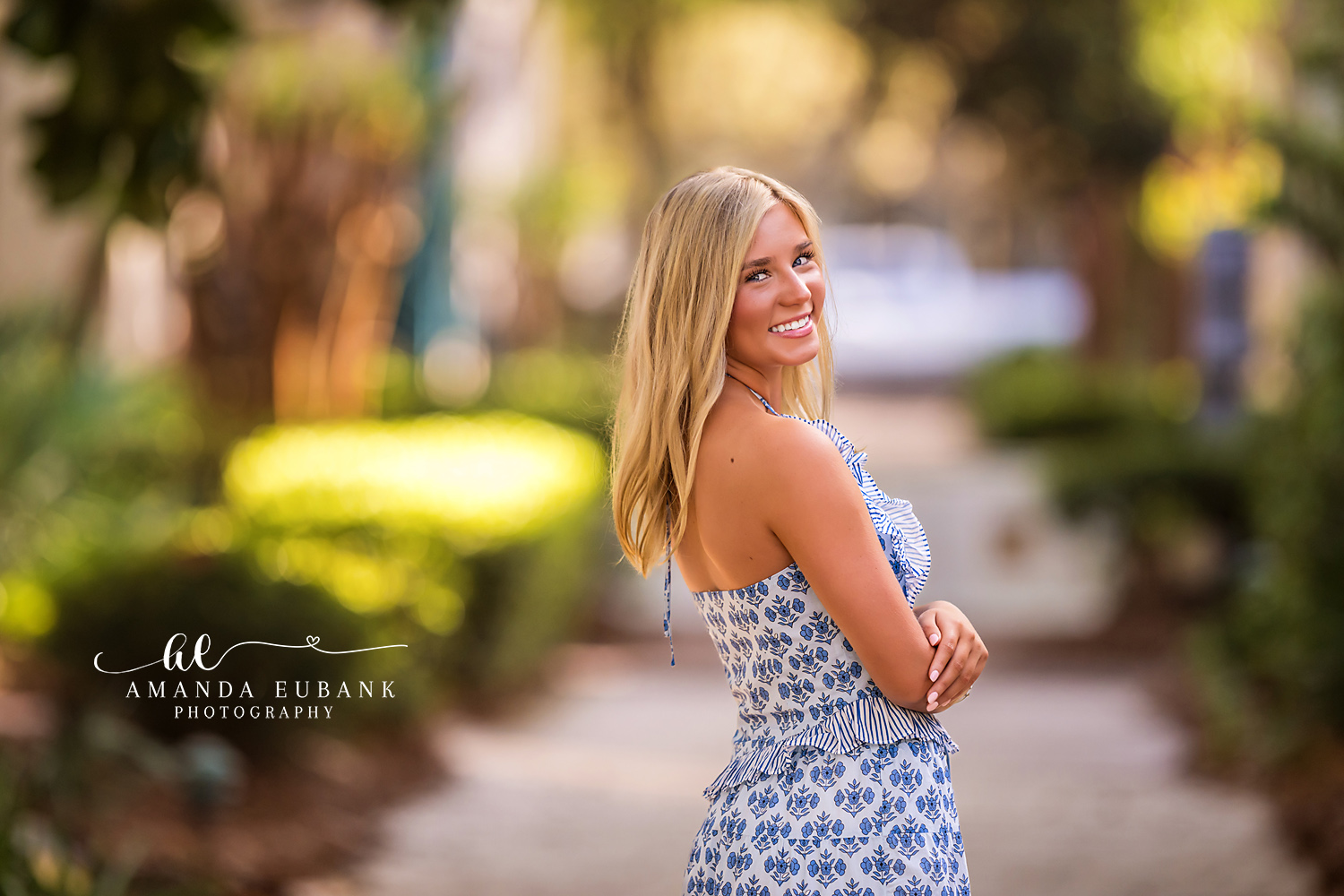 Rosemary Beach Bokeh Senior Portrait | 30A Senior Photographer Close-up senior portrait of a smiling girl glancing back over her shoulder against a dreamy bokeh background in Rosemary Beach FL