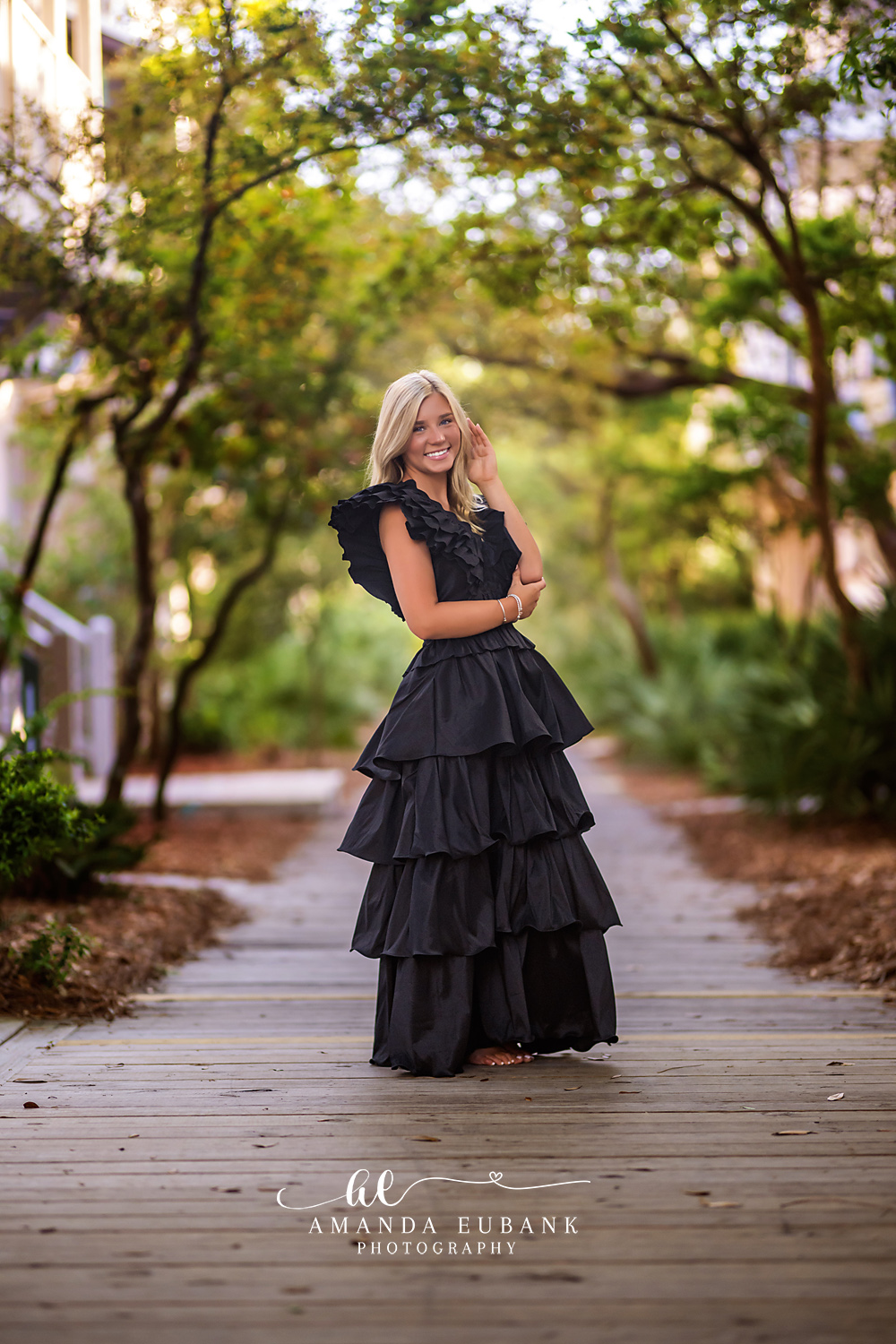 Rosemary Beach Live Oak Boardwalk Senior Portrait | 30A Senior Photographer Senior girl in a dramatic black tiered ruffle gown standing on a Rosemary Beach boardwalk under an arching canopy of live oaks