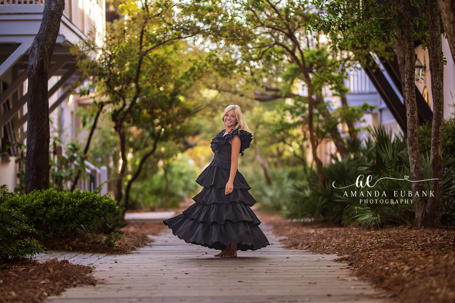 Senior girl twirling in a flowing black tiered ruffle gown on a Rosemary Beach boardwalk beneath live oak trees