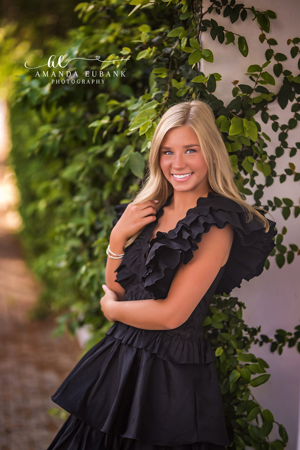 Rosemary Beach Ivy Wall Senior Portrait | 30A Senior Photographer Senior portrait of a girl in a black ruffle gown smiling against a lush ivy and vine-covered wall in Rosemary Beach FL