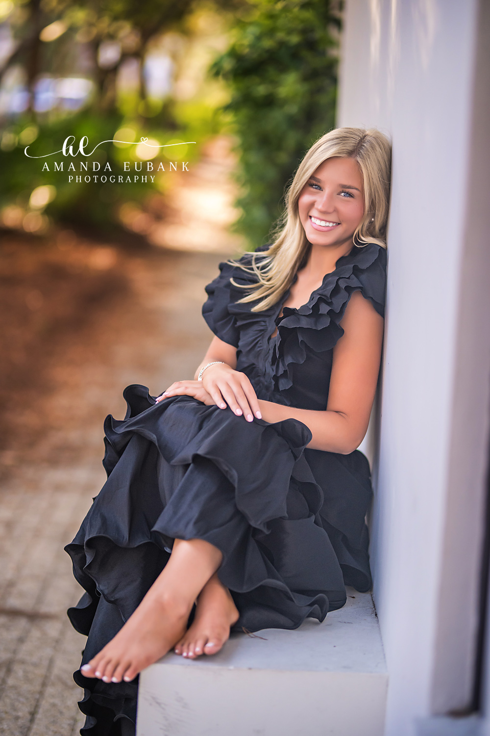 Rosemary Beach Stone Steps Senior Portrait | 30A Senior Photographer Senior girl in a black ruffle gown sitting barefoot on stone steps in Rosemary Beach FL with golden bokeh light behind her