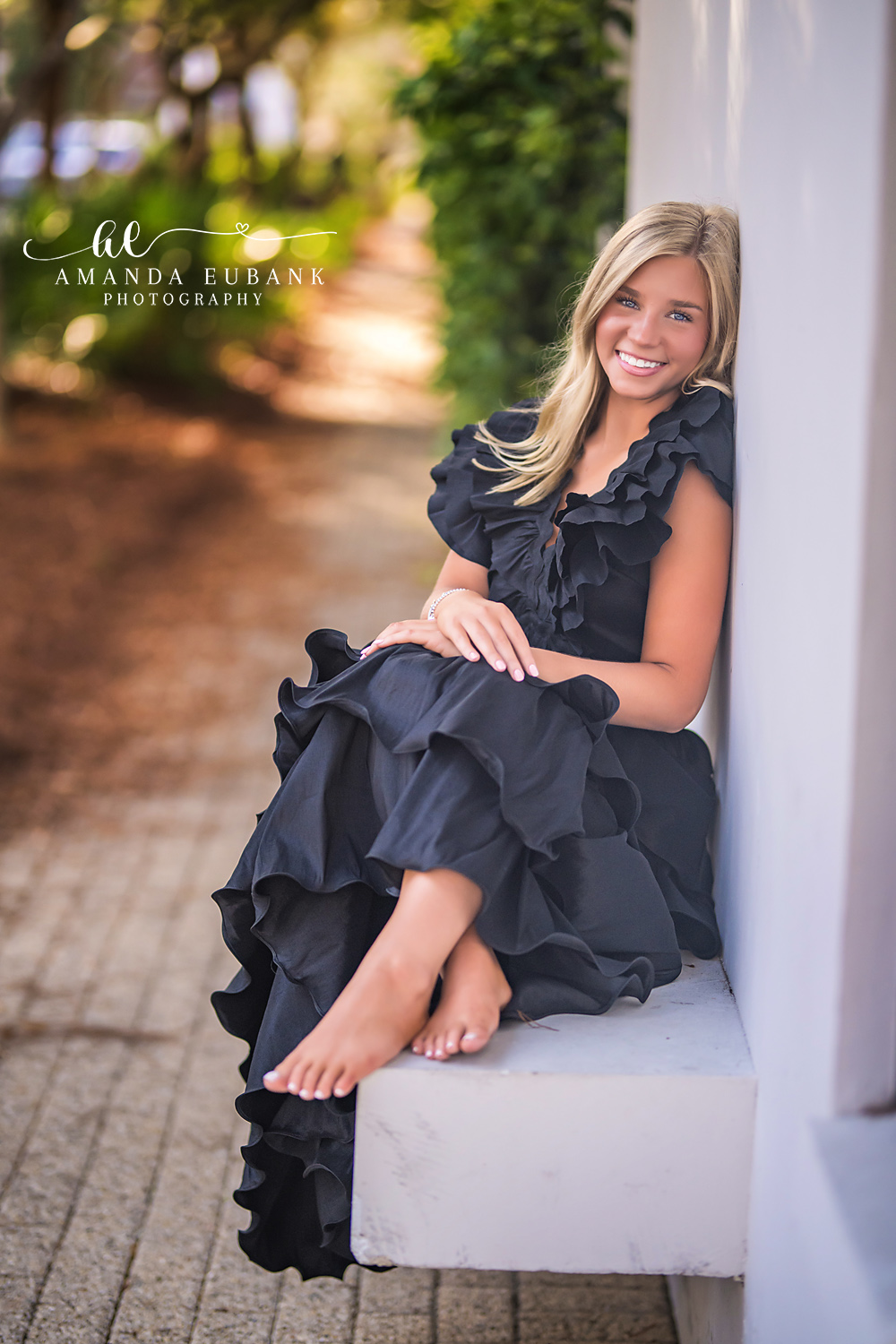 Rosemary Beach Stone Bench Senior Portrait | 30A Senior Photographer Senior girl in a black ruffle gown sitting barefoot on a stone bench in Rosemary Beach FL with crossed ankles