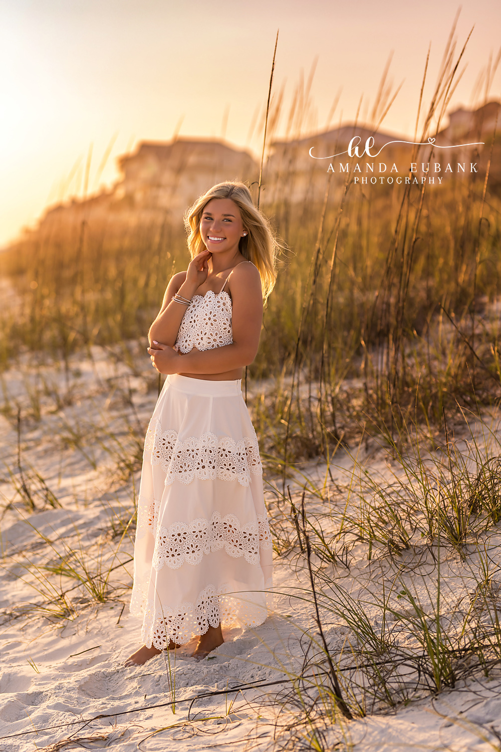 Rosemary Beach Sea Oats Golden Hour Senior Portrait | 30A Senior Photographer Senior girl in a white eyelet two-piece set standing among sea oats in the dunes at golden hour on Rosemary Beach FL