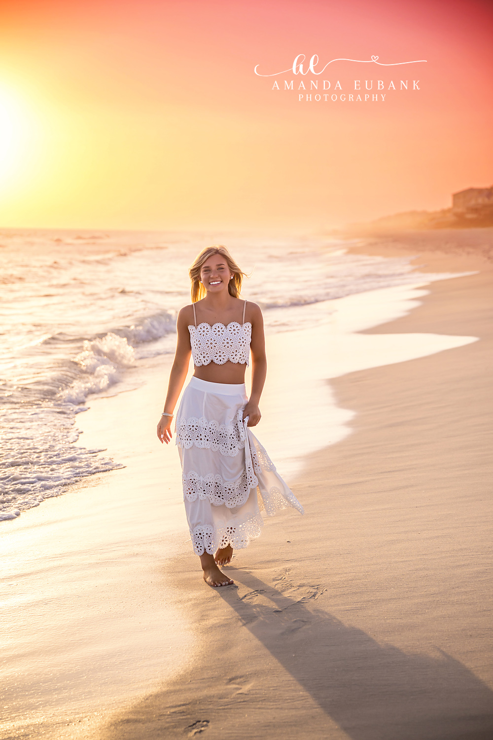Rosemary Beach Footprints Sunset Senior Portrait | 30A Senior Photographer Senior girl in white eyelet outfit walking on the Rosemary Beach shoreline at sunset with footprints trailing behind her