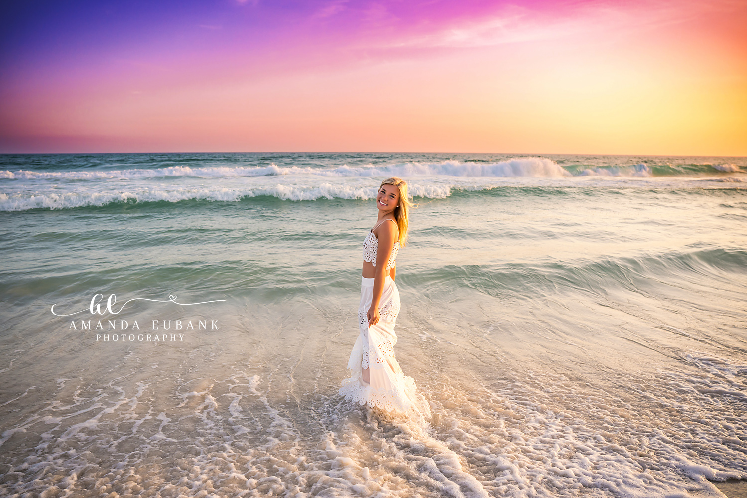 Rosemary Beach Dramatic Sunset Senior Portrait | 30A Senior Photographer Senior girl in white eyelet two-piece standing in the Gulf surf at Rosemary Beach beneath a dramatic purple, pink, and orange sunset sky