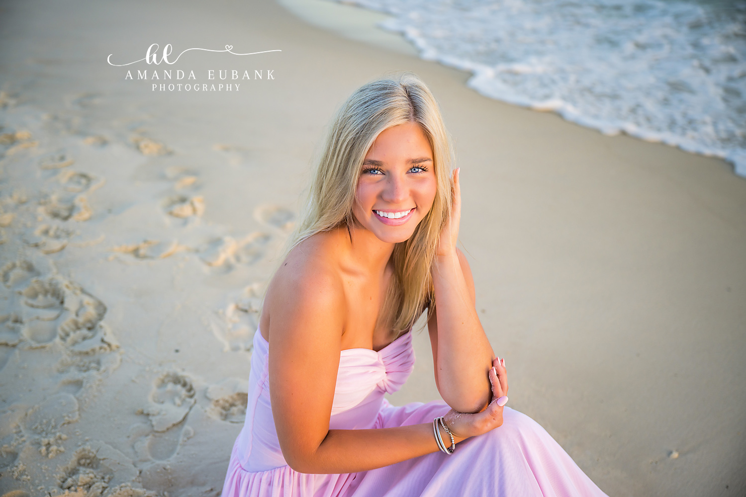 Rosemary Beach Shoreline Close-Up Senior Portrait | 30A Senior Photographer Close-up senior portrait of a smiling girl in a blush pink gown kneeling on the Rosemary Beach shoreline as a Gulf wave rolls in behind her