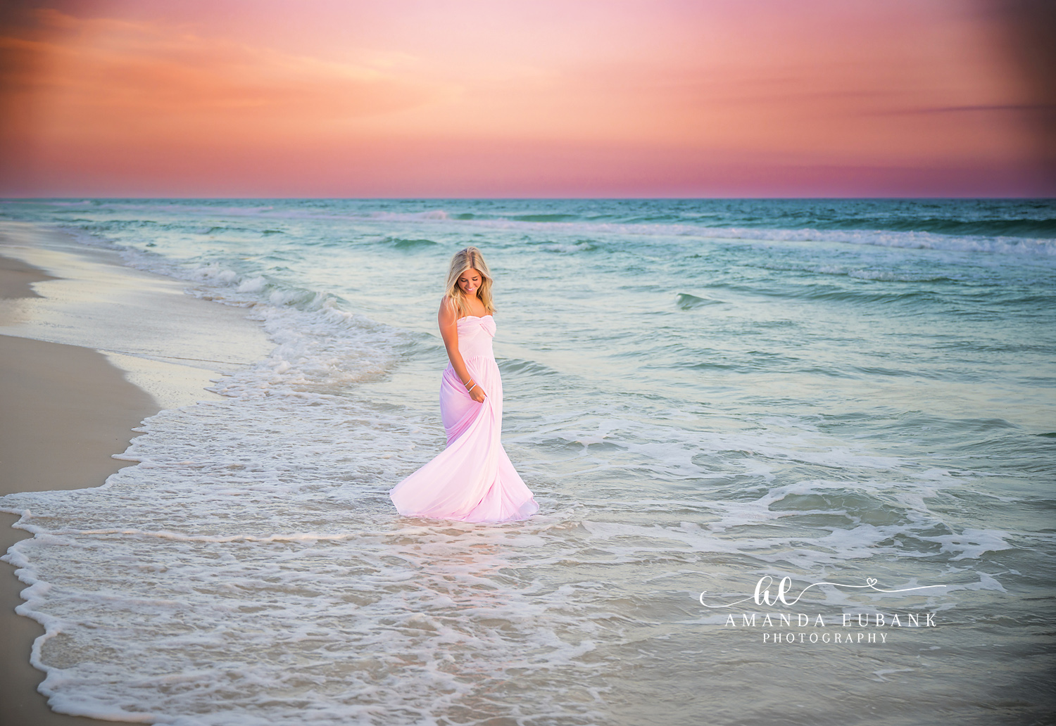 Rosemary Beach Painterly Sunset Senior Portrait | 30A Senior Photographer Senior girl in a flowing blush pink gown standing in the turquoise Gulf surf at Rosemary Beach beneath a pastel coral sunset sky