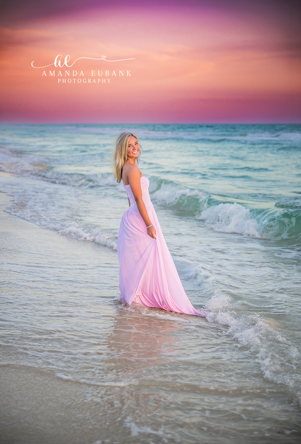 Rosemary Beach Sunset Gown in the Surf Senior Portrait | 30A Senior Photographer Senior girl in a flowing blush pink gown standing in the turquoise Gulf surf at Rosemary Beach beneath a soft purple and pink sunset sky