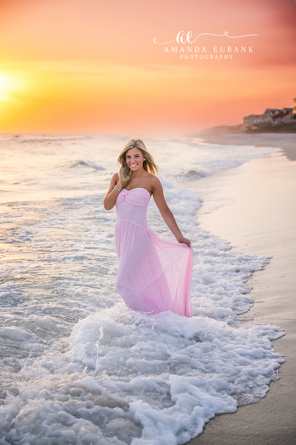 Rosemary Beach Sunset Surf Senior Portrait | 30A Senior Photographer High school senior in a flowing blush pink gown standing in the surf at sunset on Rosemary Beach FL with the Gulf horizon glowing behind her