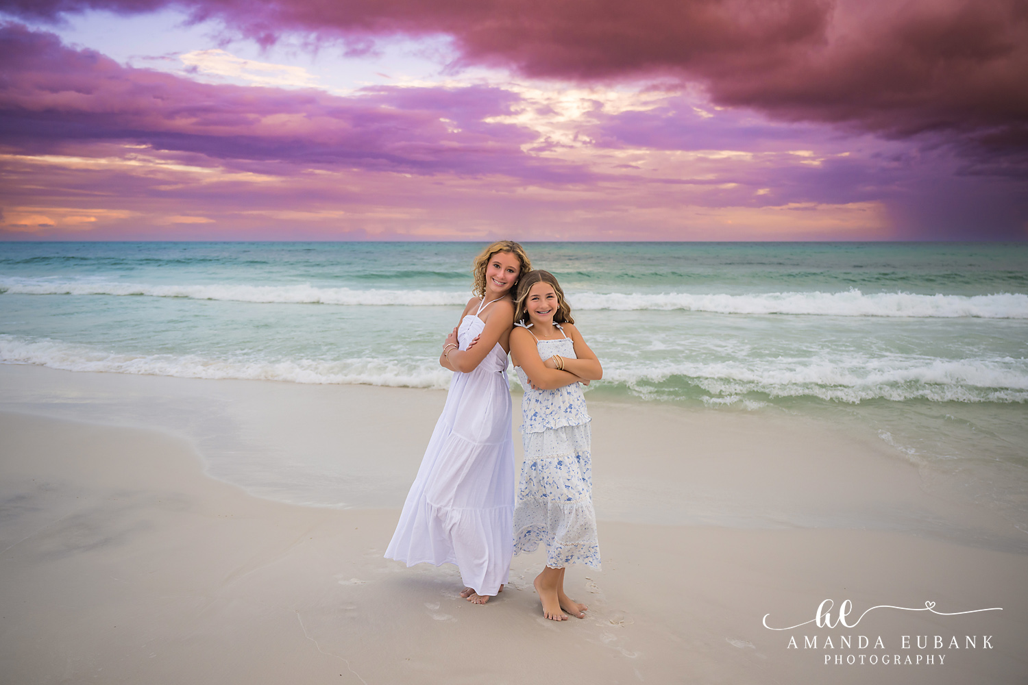 Santa Rosa Beach Family Photos – Mother and Daughter at Sunset Two girls in white dresses hugging on the sand as the 30A sunset sky turns pink and violet