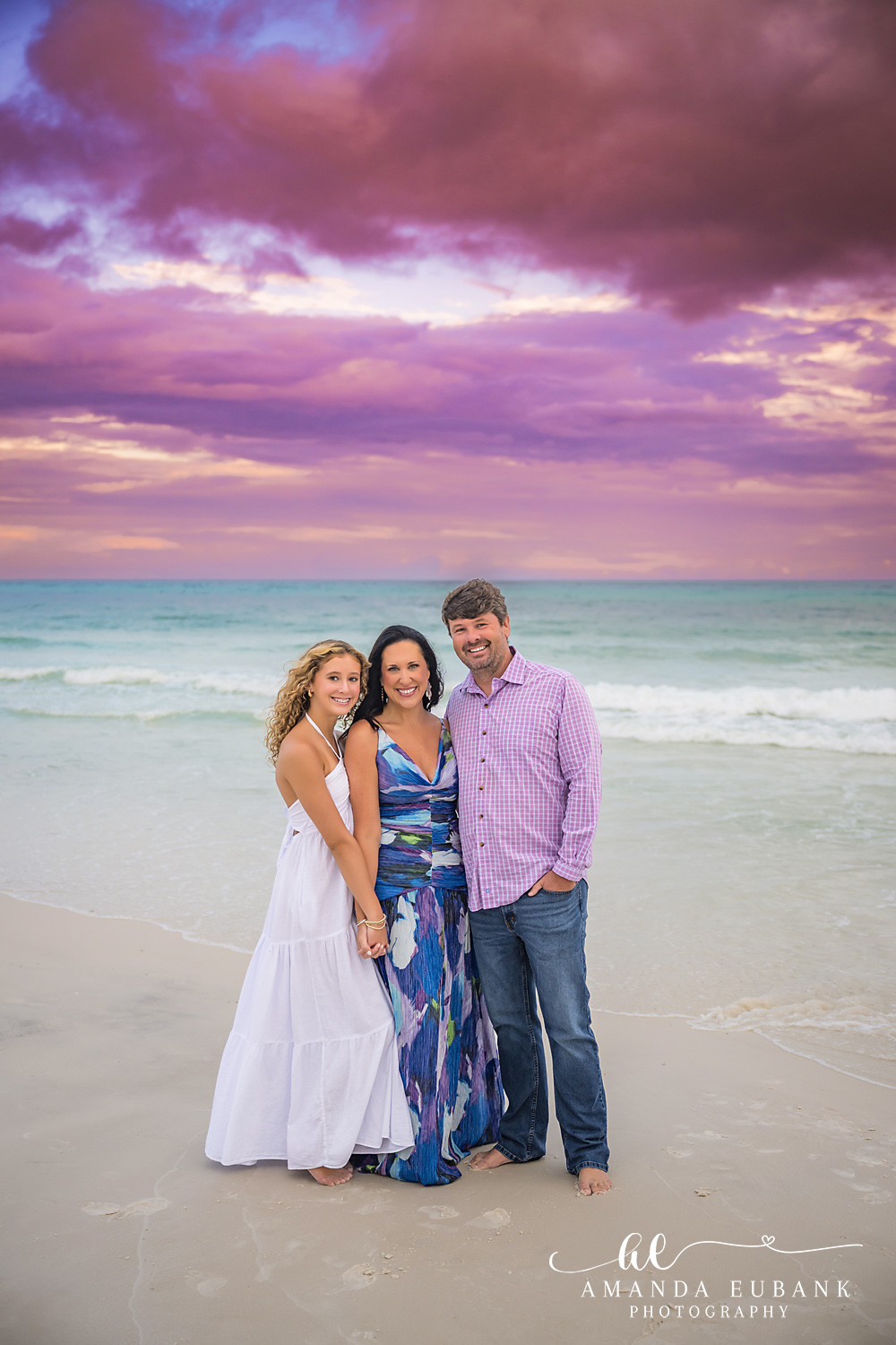 Santa Rosa Beach Family Photographer – Sunset Portrait on 30A Three family members close together on 30A at sunset with emerald water and violet clouds behind