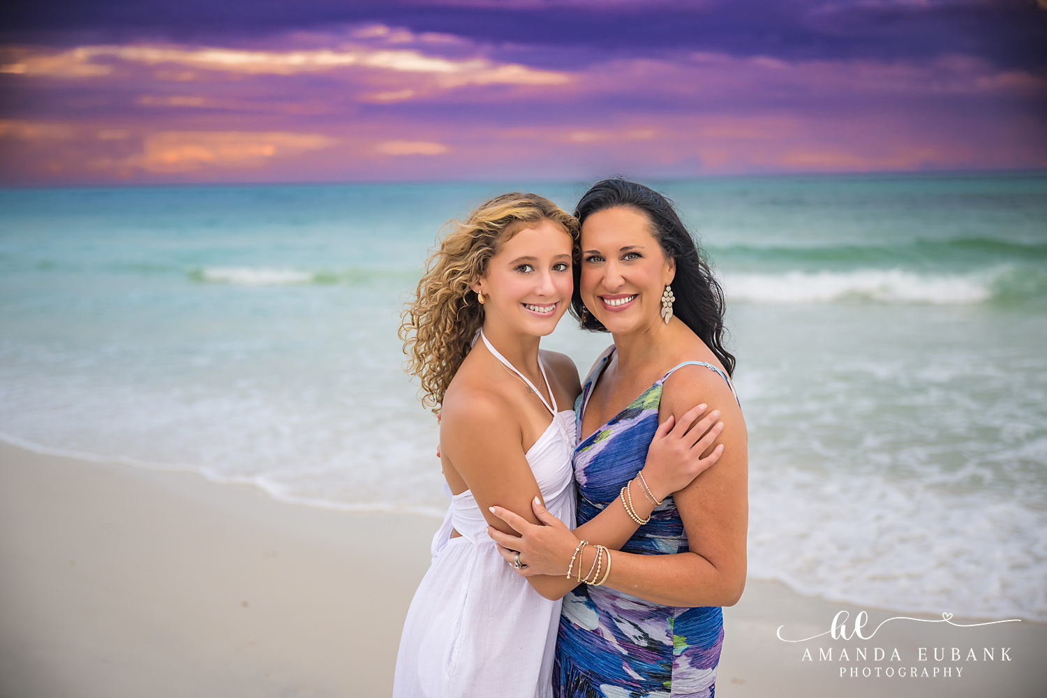 Mother and Daughter Beach Portrait on 30A – Santa Rosa Beach Teen in a white maxi dress hugging a woman in a blue floral dress on the 30A shoreline