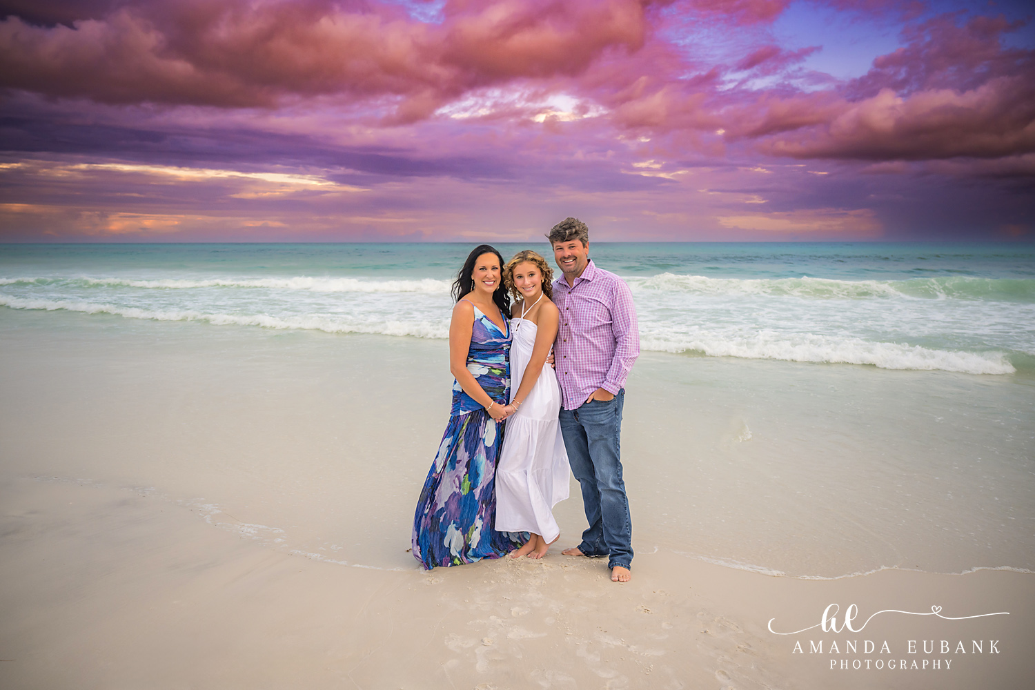 Santa Rosa Beach Family Portrait Session on 30A Three family members barefoot on the sand as the 30A sunset sky glows lavender and rose