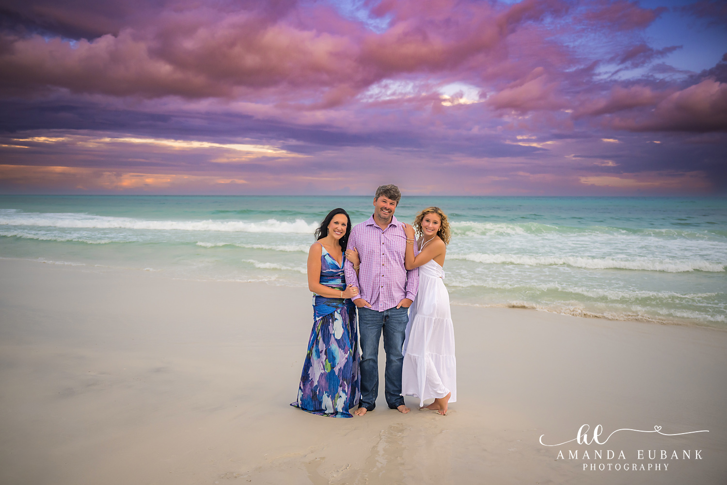 Wide 30A beach portrait with a dramatic violet sunset sky filling the frame above the family