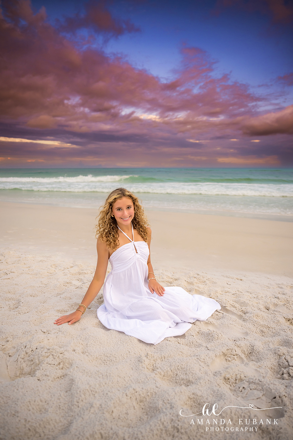 30A Senior and Teen Beach Portrait in Santa Rosa Beach Teen girl in a white maxi dress seated on the sugar-white sand at sunset on 30A