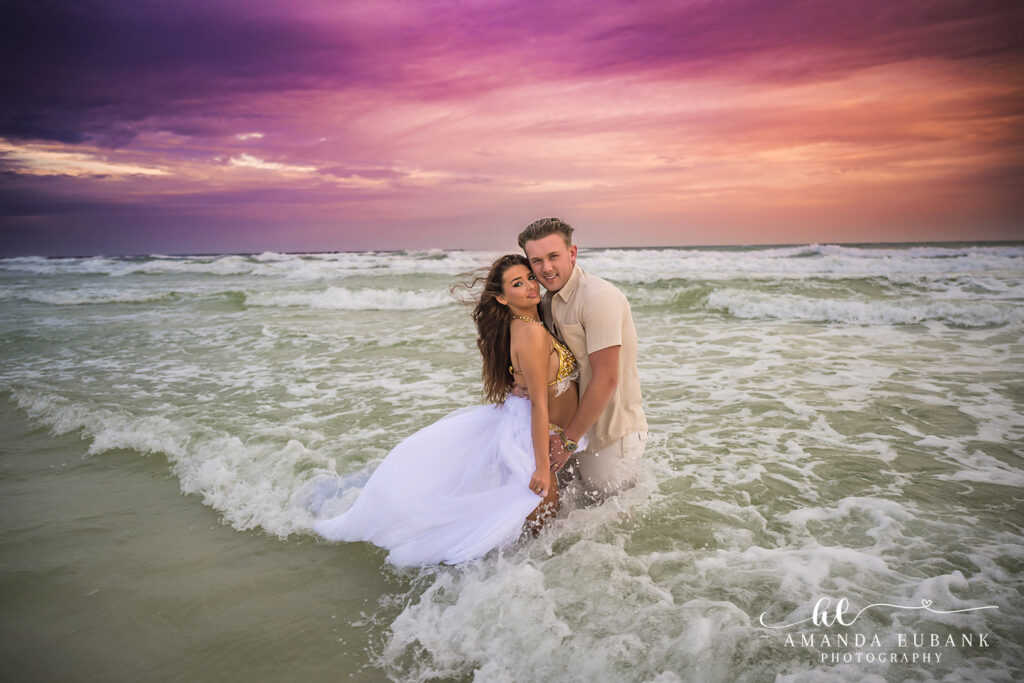 Couple laughing in the surf as a wave breaks around them during a 30A sunset session