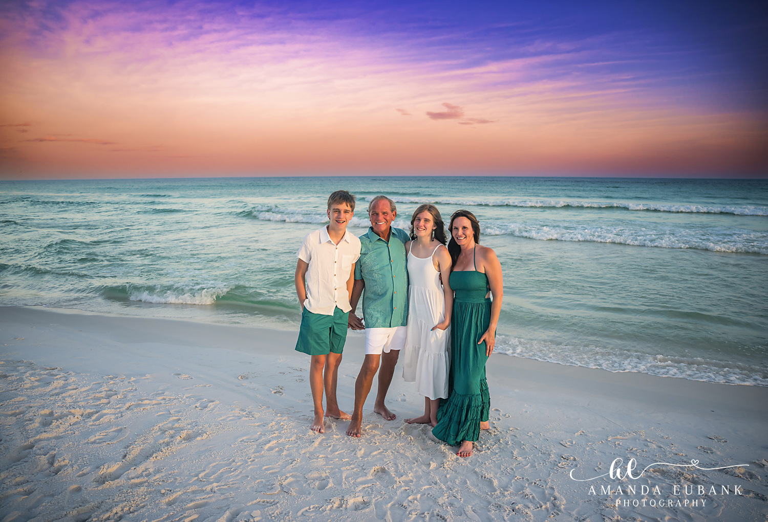 Destin Family Photographer – Family Portrait at the Water’s Edge Family of four standing at the water's edge in Destin, Florida during sunset