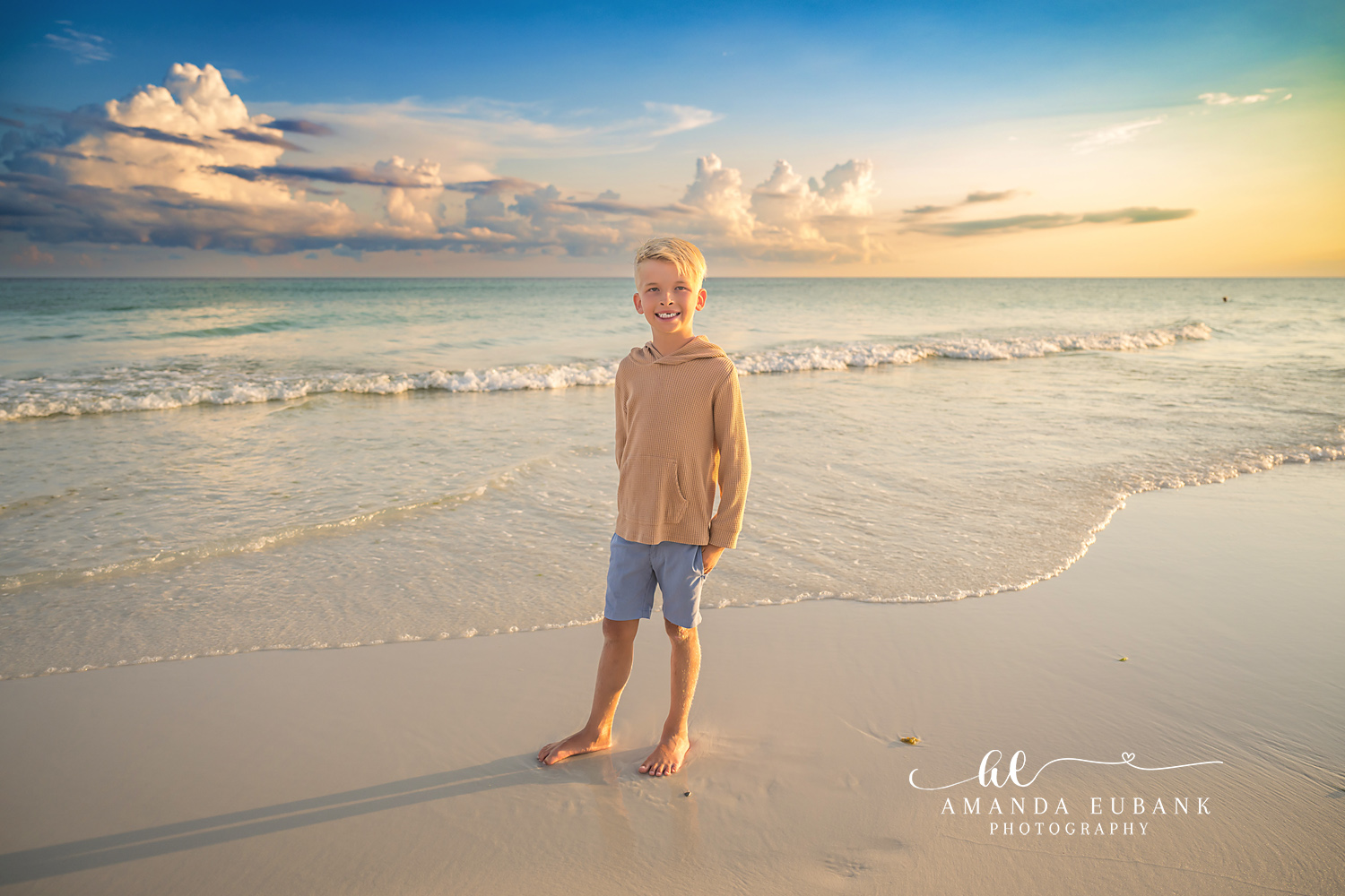 Destin Beach Family Session – Boy Standing on the Shoreline Young boy in a tan hoodie and blue shorts standing on the shoreline at sunset during a Destin family photography session