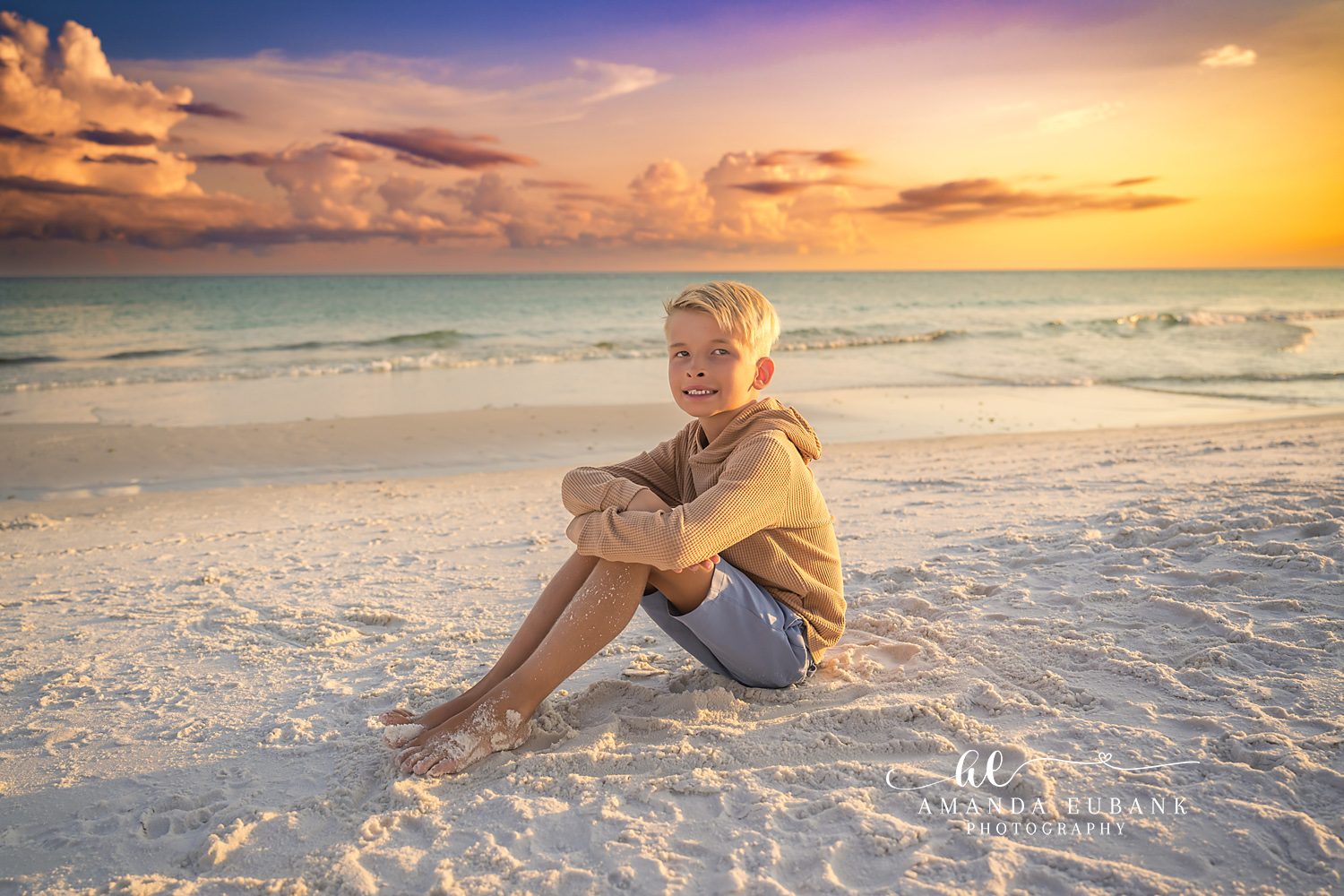 Destin Beach Family Session – Sunset Portrait in the Sand Young boy in a tan hoodie sitting in the white sand at sunset during a Destin beach family photography session