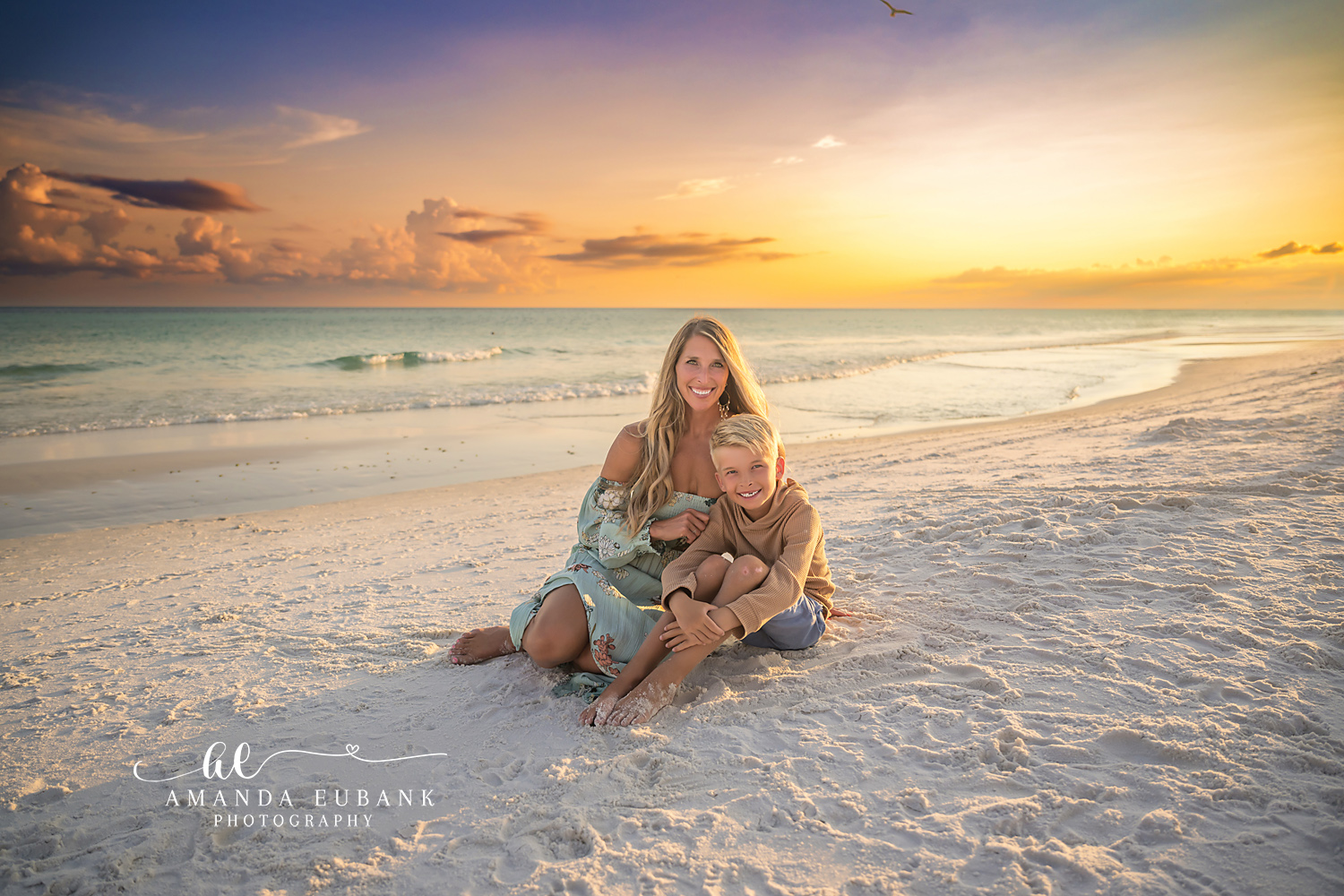 Destin Beach Family Session – Mother and Son in the Sand Mother in a green dress sitting in the sand with her arms around her son at sunset during a Destin family photography session