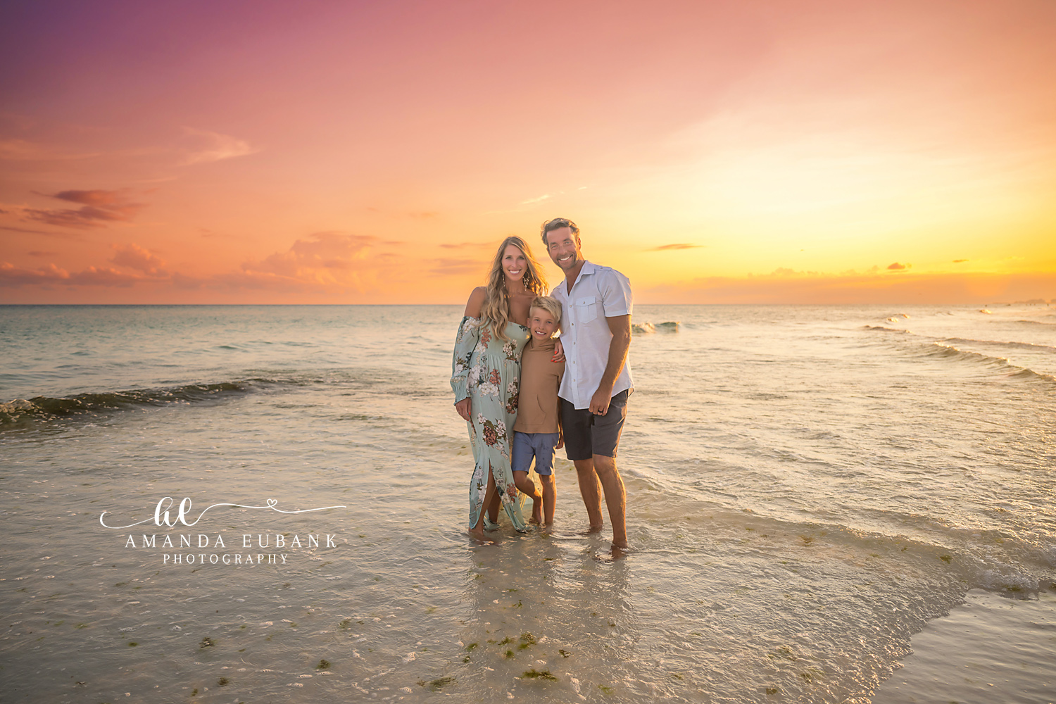 Destin Beach Family Session – Family Portrait at the Water’s Edge Family of three standing together at the water's edge at sunset during a Destin beach family photography session