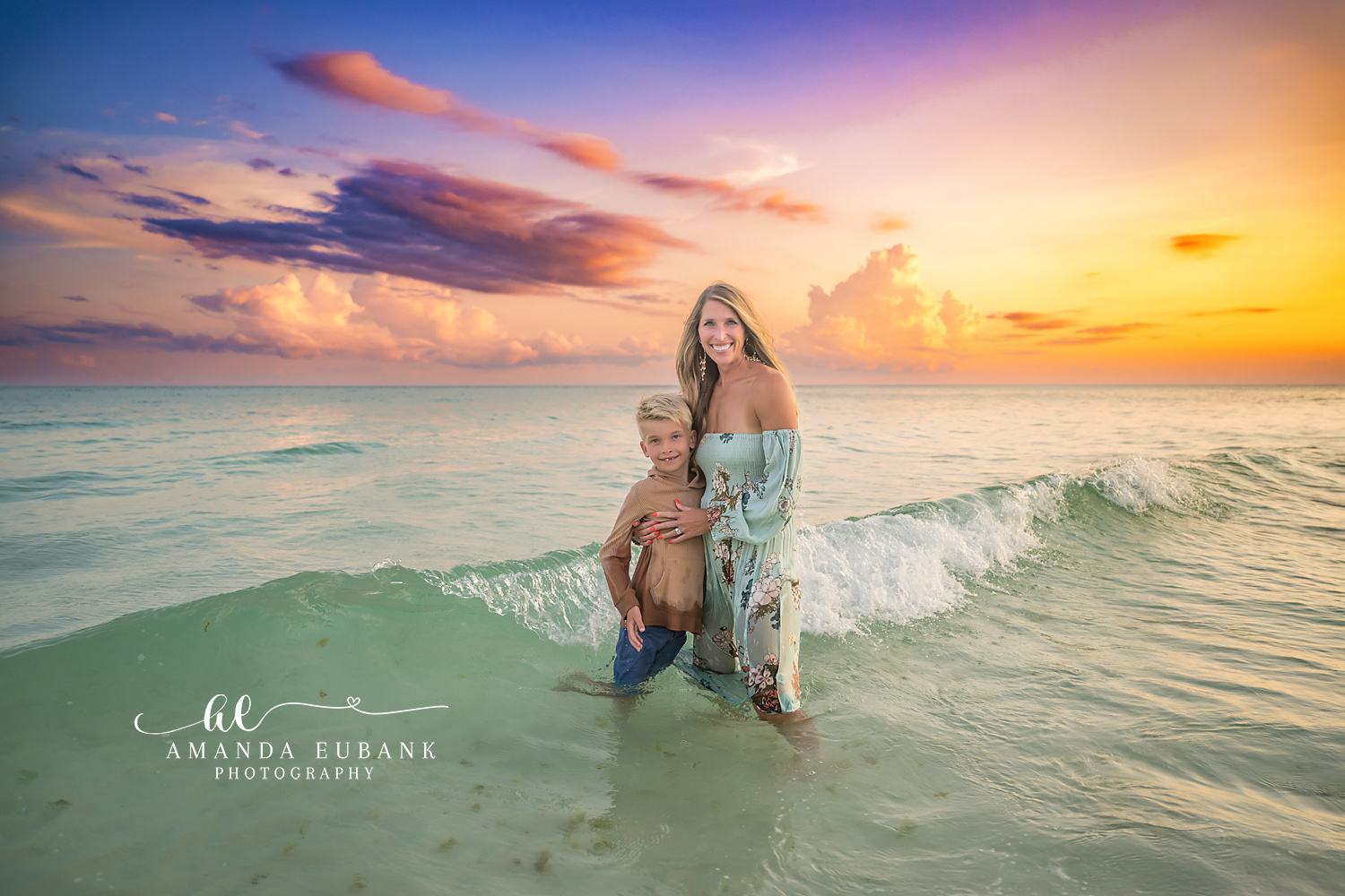 Destin Beach Family Session – Mother and Son Embrace in the Surf Mother in a floral dress standing in the surf with her young son holding onto her at sunset in Destin