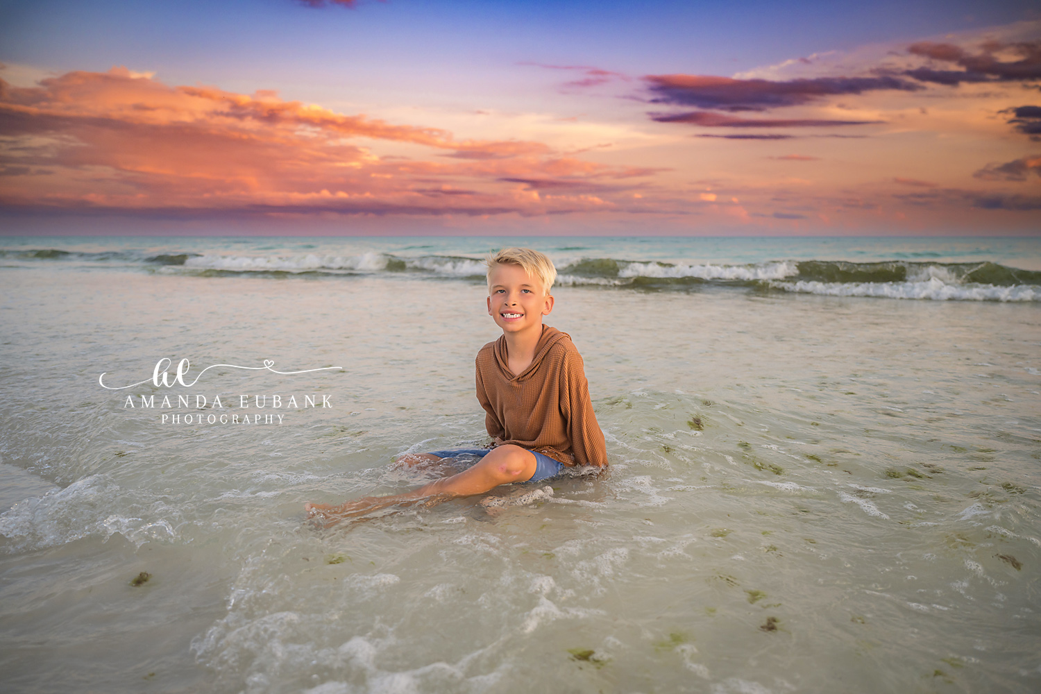 Destin Beach Family Session – Playing in the Shallow Surf Young boy playing in the shallow surf beneath a pink and purple sunset during a Destin beach family photography session