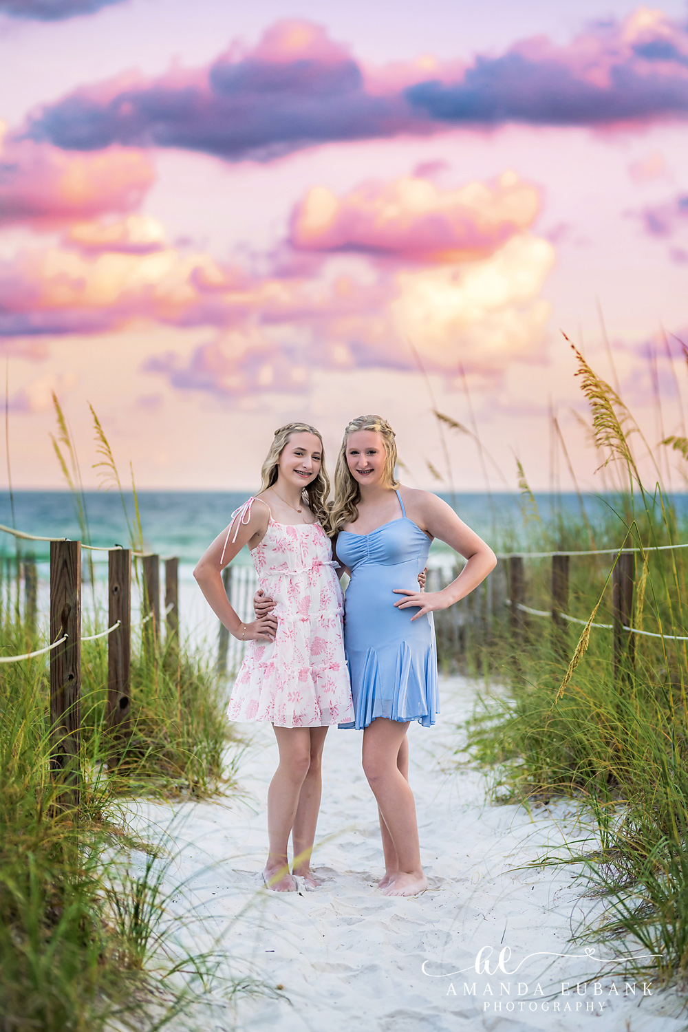 Destin Beach Family Photos – Sisters on the Dune Walkover Two girls in pink and periwinkle dresses by the dune fence and sea oats at sunset in Destin