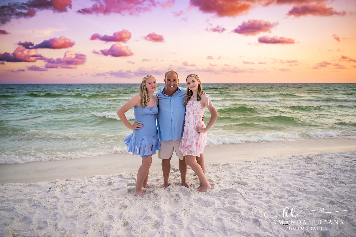 Destin Family Beach Photos – Dad with His Daughters Wide Destin beach portrait of three family members with the Gulf and pink clouds behind them
