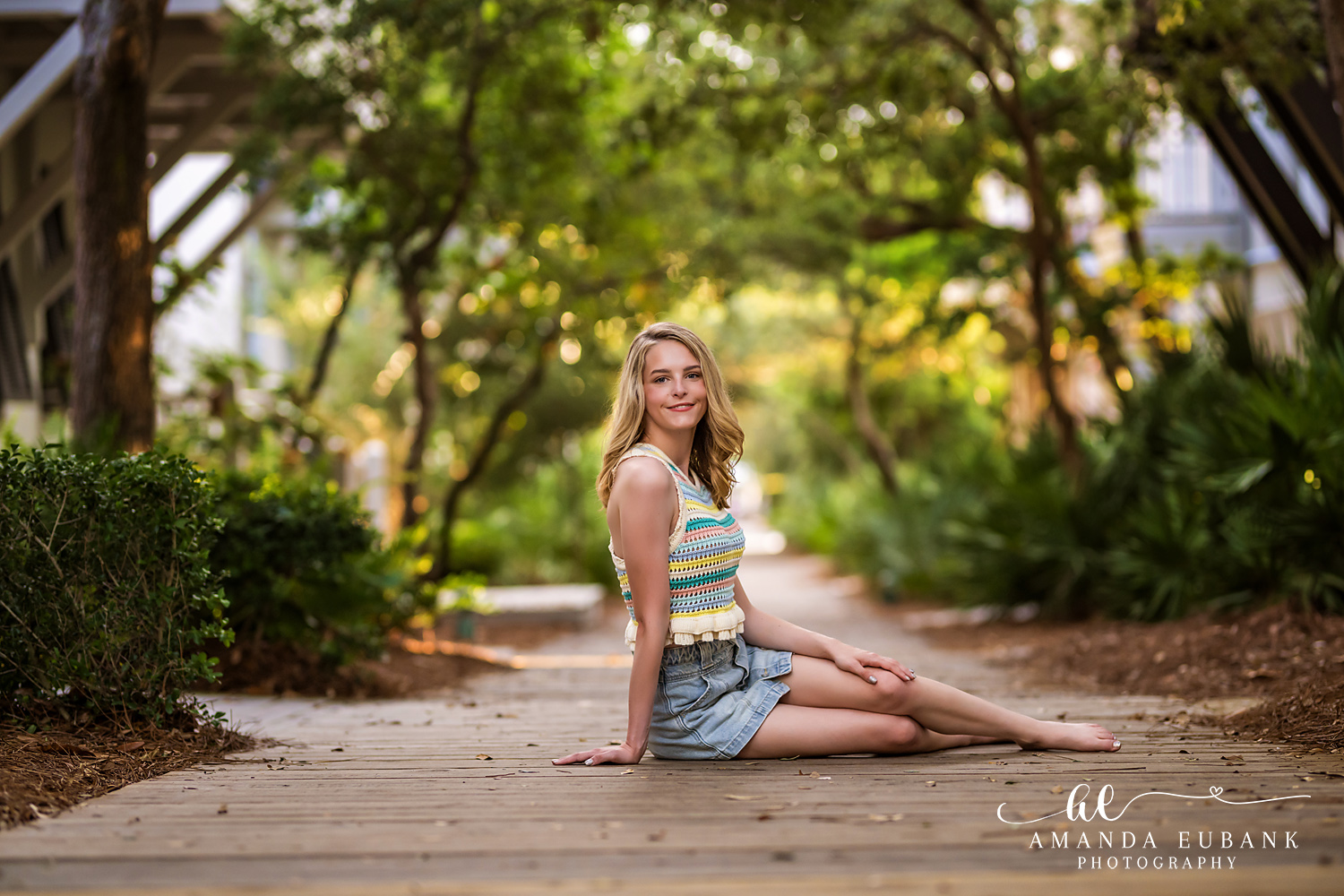Rosemary Beach Senior Photographer – Boardwalk Portrait in the Garden Senior girl in a striped top and denim skirt sitting on a wooden boardwalk in Rosemary Beach, Florida