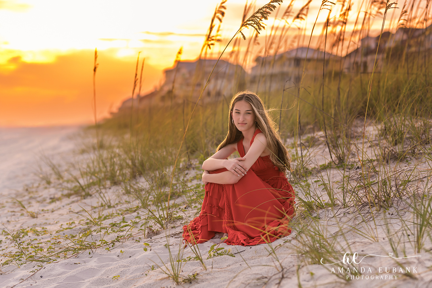 Senior girl in a red dress sitting among the sand dunes at sunset in Rosemary Beach, Florida