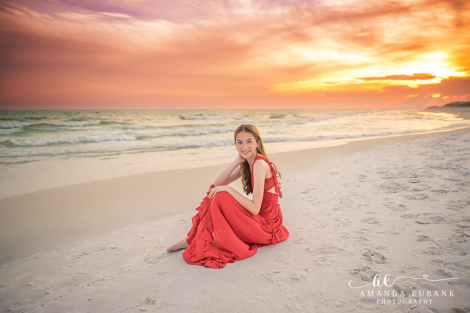 Rosemary Beach Senior Photographer – Seated on the Shoreline Senior girl in a red dress sitting on the sand at the shoreline in Rosemary Beach, Florida