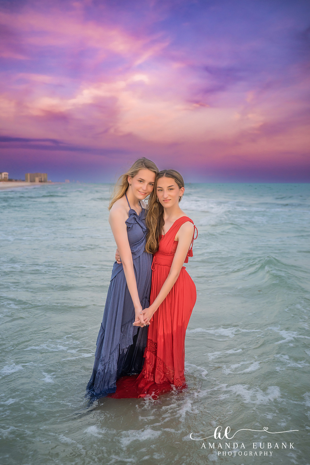 Rosemary Beach Senior Photographer – Two Seniors at Twilight Two senior girls in red and navy dresses standing together in the ocean at twilight in Rosemary Beach, Florida