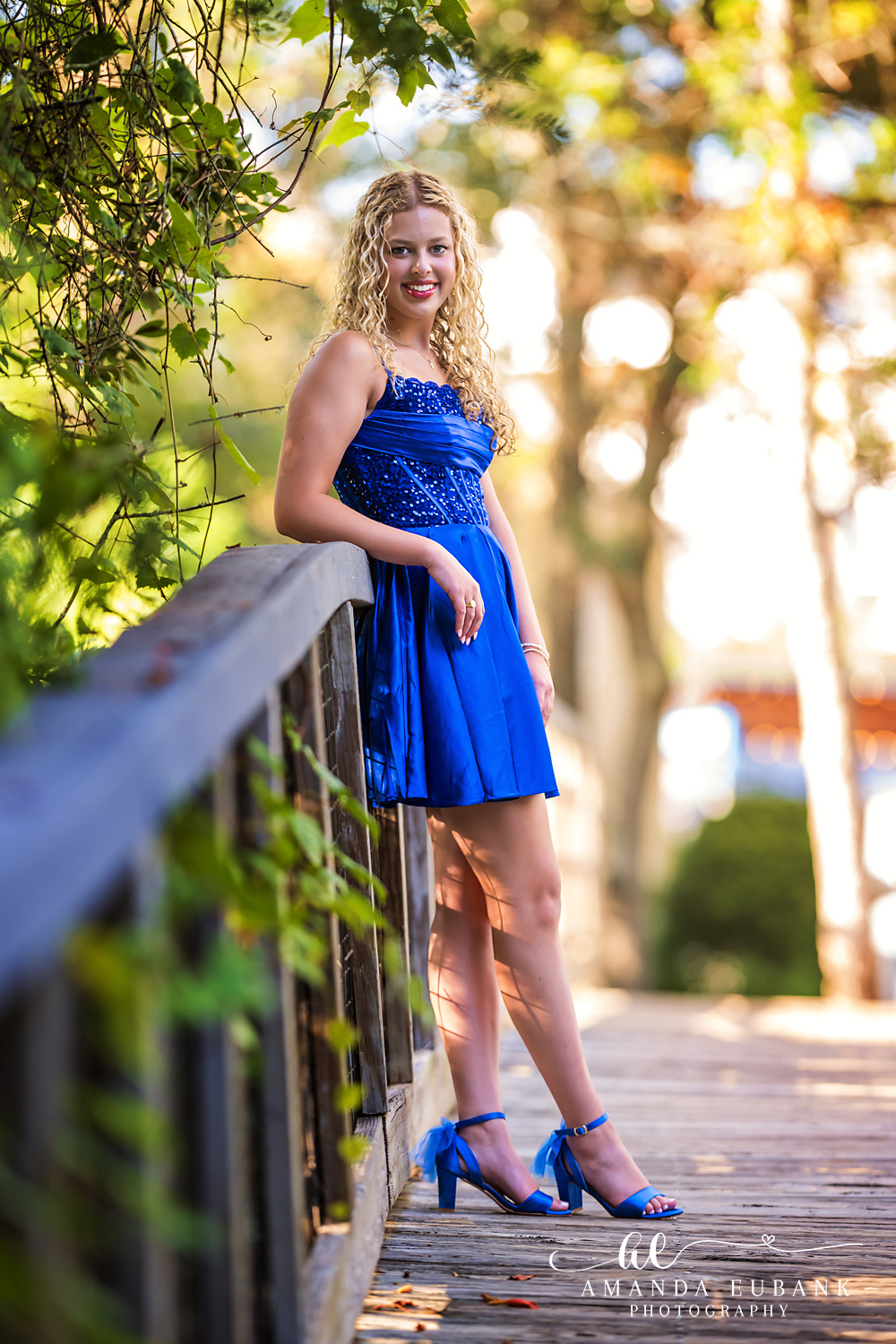 Sandestin Senior Photographer – Boardwalk Railing Portrait Senior girl in a blue dress leaning on a wooden boardwalk railing in Sandestin, Florida