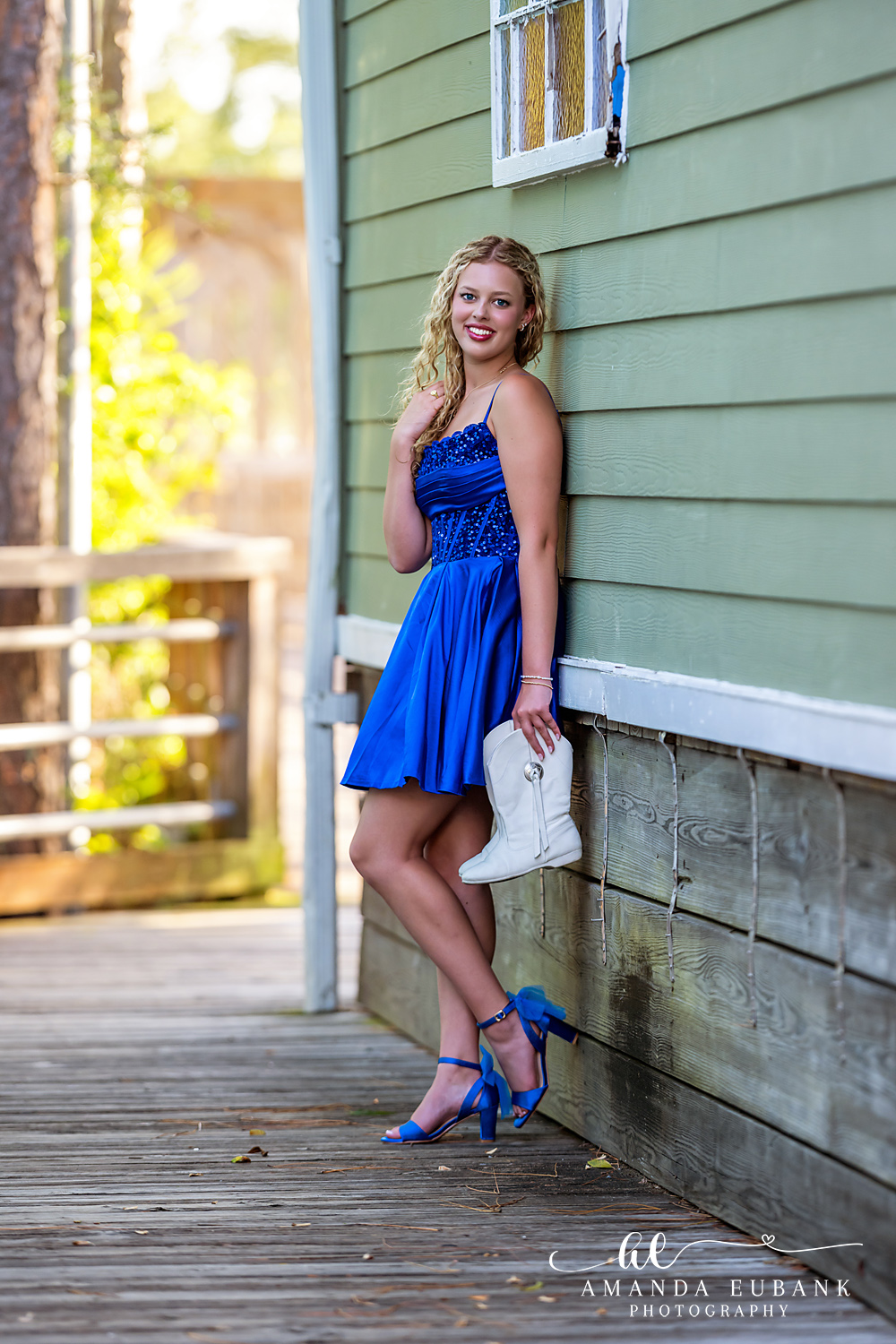 Sandestin Senior Photographer – Portrait by the Turquoise Cottage Senior girl in a blue dress standing beside a turquoise beach cottage wall in Sandestin, Florida