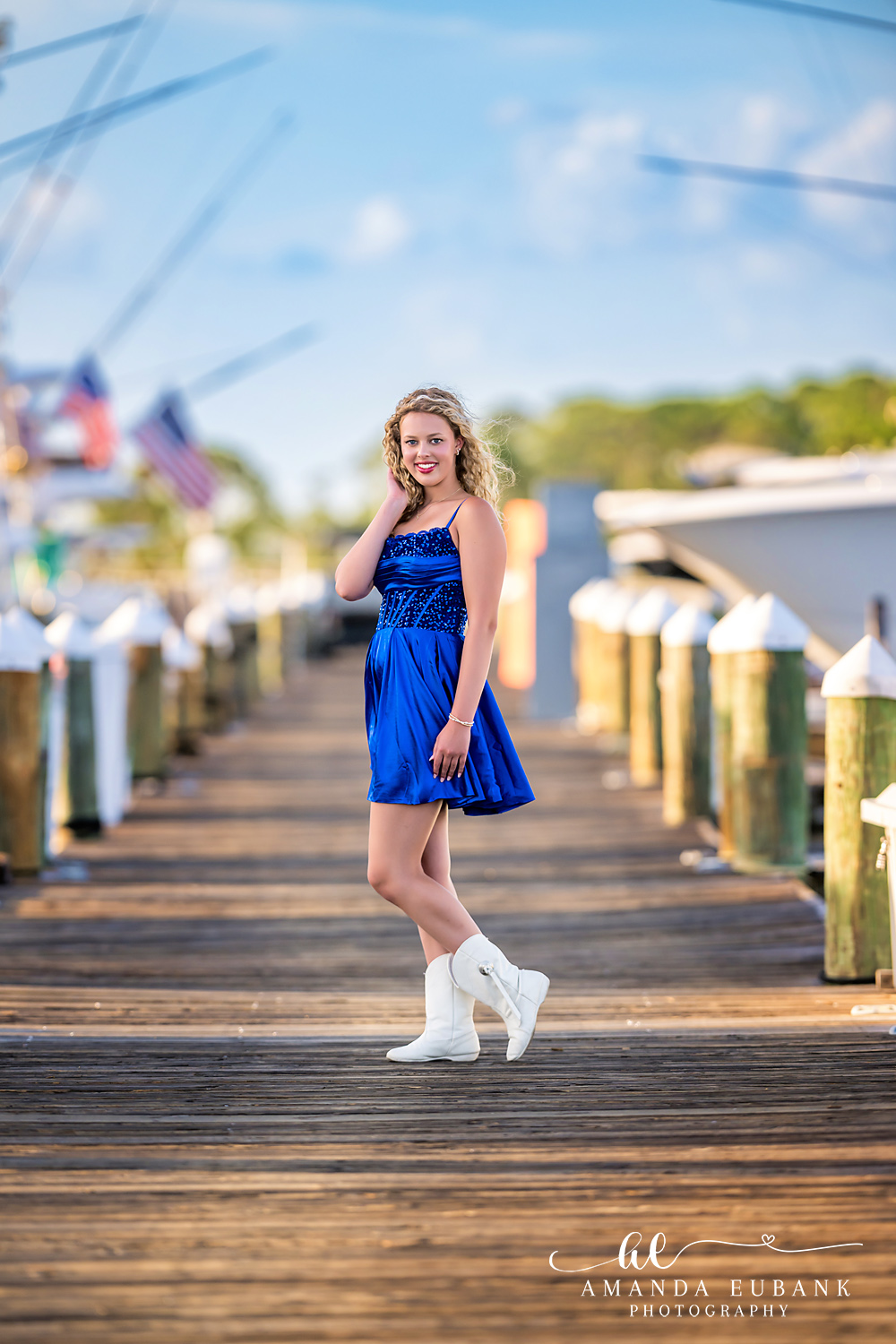 Sandestin Senior Photographer – Walking the Boardwalk at Golden Hour High school senior walking along a wooden boardwalk in a blue dress in Sandestin, Florida