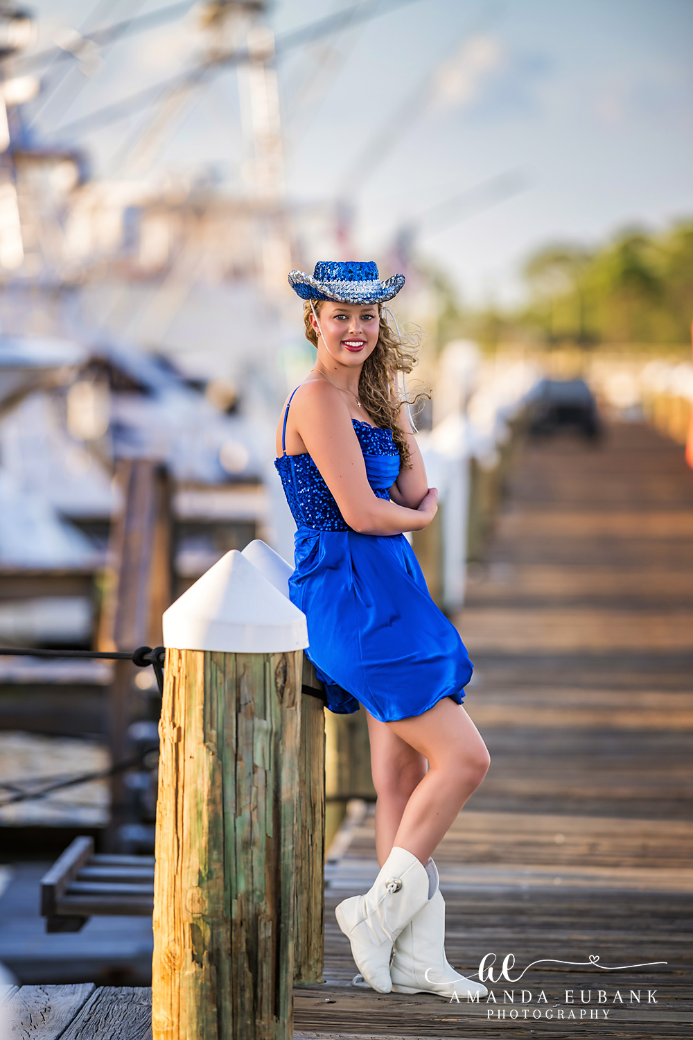 Sandestin Senior Photographer – Blue Sun Hat on the Boardwalk Senior girl in a blue dress and sun hat posing on a boardwalk railing in Sandestin, Florida