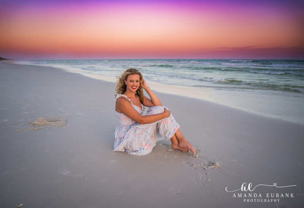 High school senior with wavy hair in a white dress standing on the beach in Sandestin, Florida