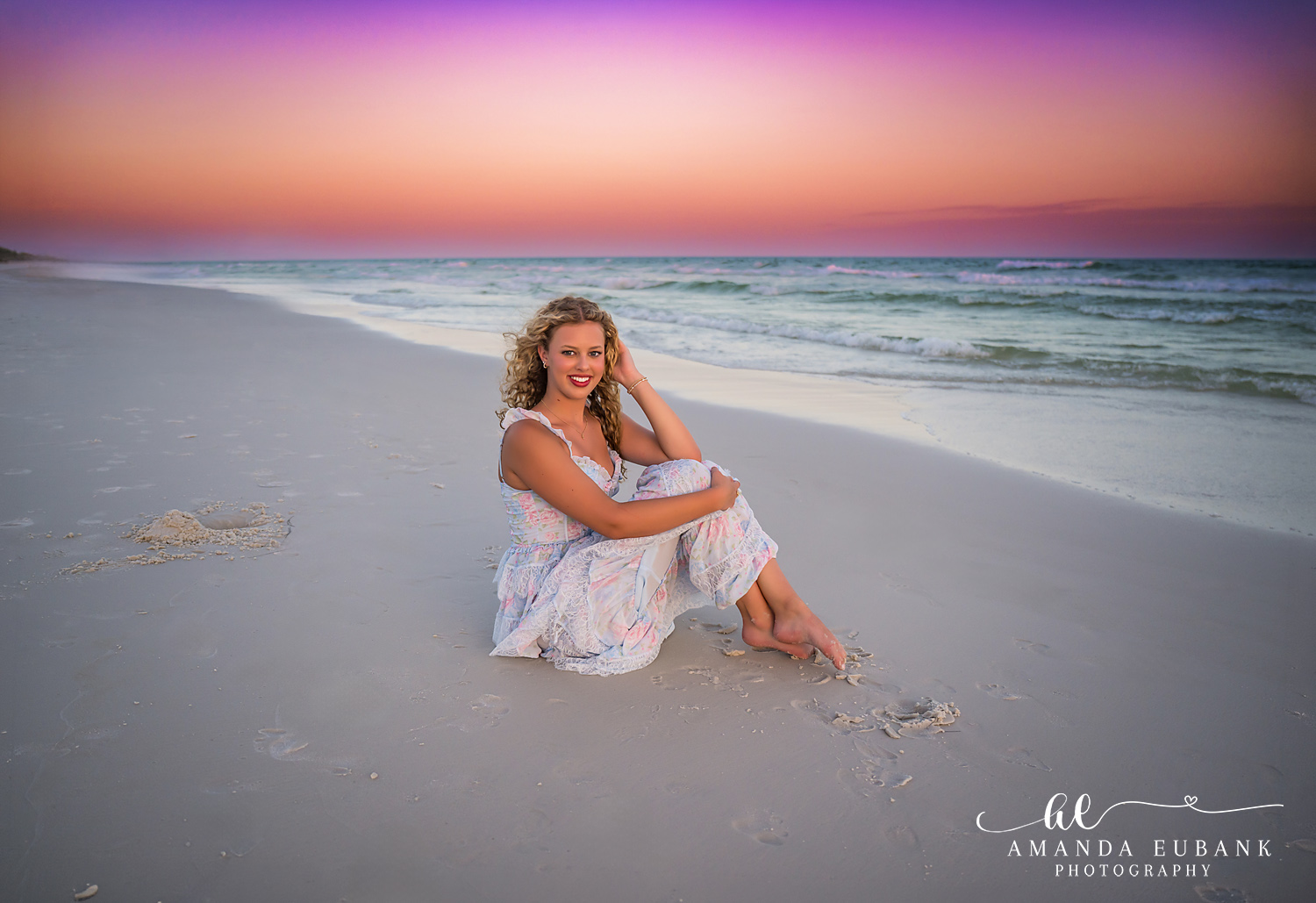 High school senior with wavy hair in a white dress standing on the beach in Sandestin, Florida