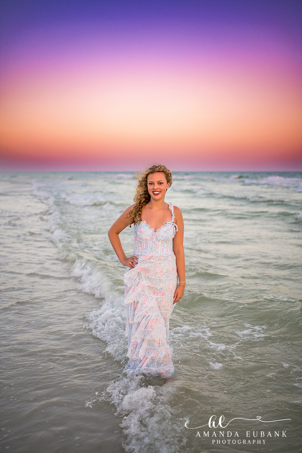 Sandestin Senior Photographer – Playful Smile at the Shoreline High school senior smiling with hand on hip at the shoreline in a white dress in Sandestin, Florida
