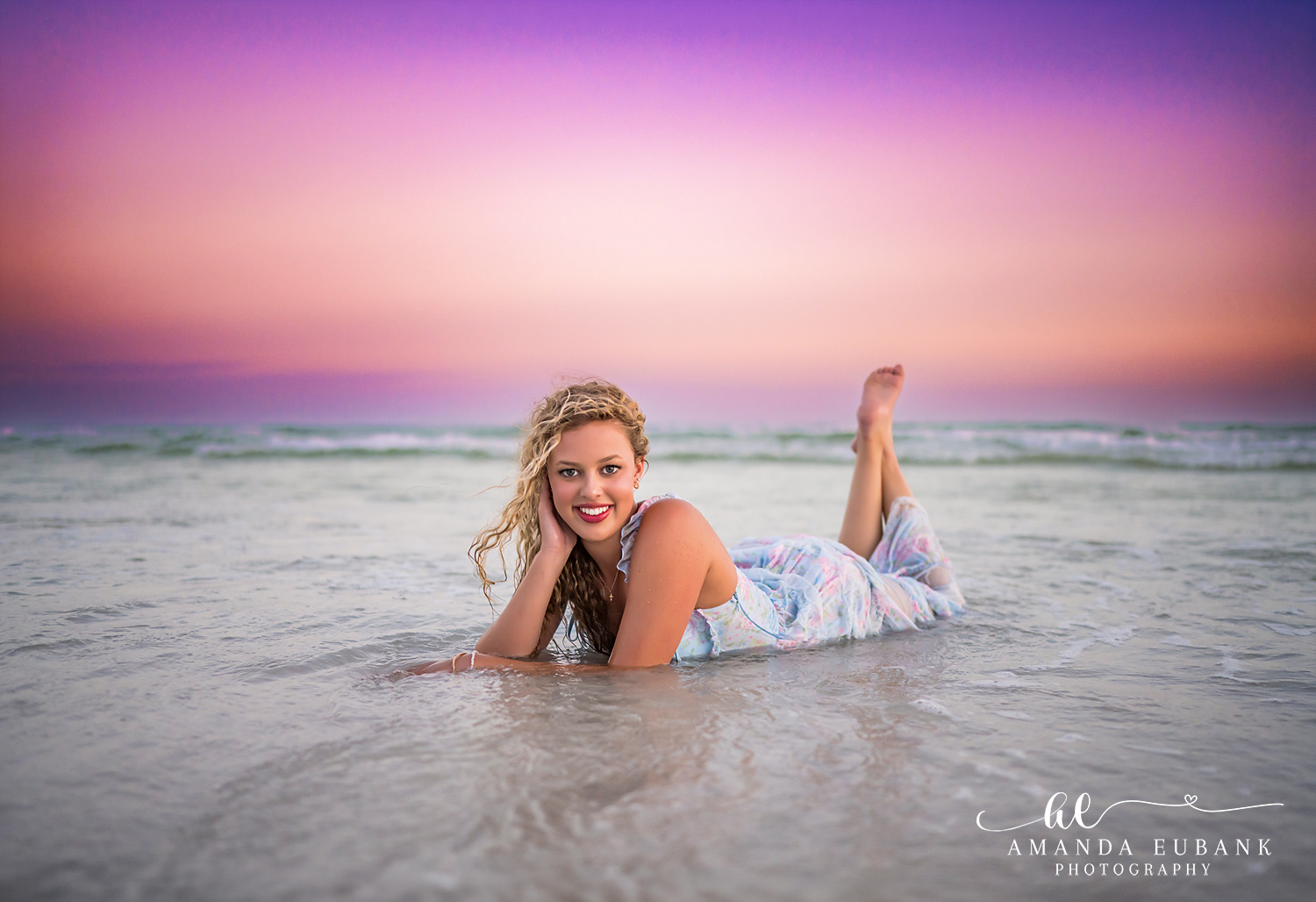 Sandestin Senior Photographer – Resting in the Shallow Waves High school senior lying in shallow ocean water in a floral dress at sunset in Sandestin, Florida