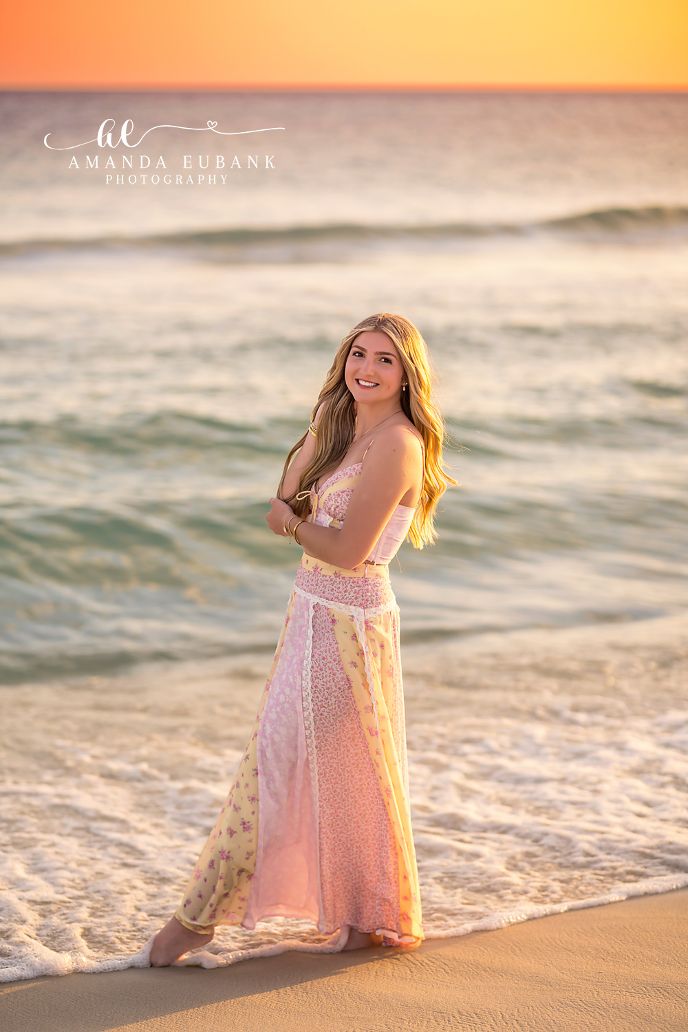 Santa Rosa Beach Senior Session – Golden Hour Portrait at the Water’s Edge High school senior in a blush lace gown smiling at the water's edge during a golden hour Santa Rosa Beach senior photography session