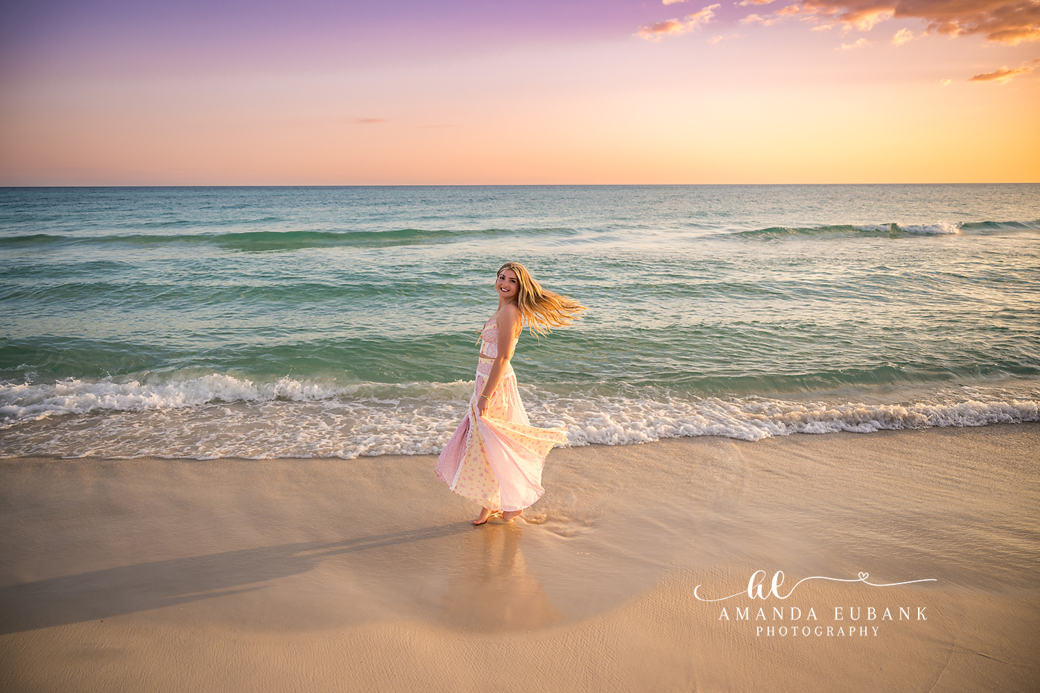 Santa Rosa Beach Senior Session – Walking the Shoreline at Sunset High school senior in a blush gown walking along the shoreline with her hair and dress in the breeze at sunset in Santa Rosa Beach