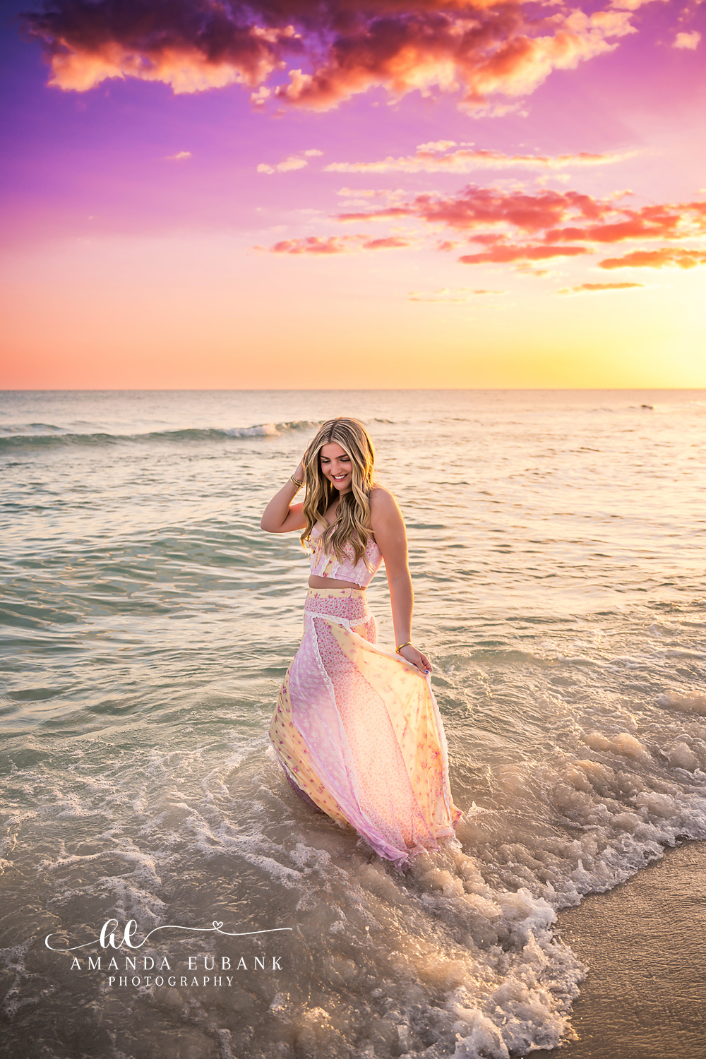 Santa Rosa Beach Senior Session – Pink and Purple Sunset Portrait High school senior in a blush lace gown standing in the surf beneath pink and purple sunset clouds at Santa Rosa Beach