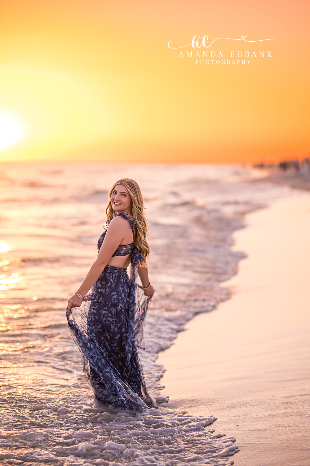 Santa Rosa Beach Senior Session – Looking Back at Golden Hour High school senior in a navy floral gown looking back over her shoulder in the surf under a glowing orange sunset at Santa Rosa Beach