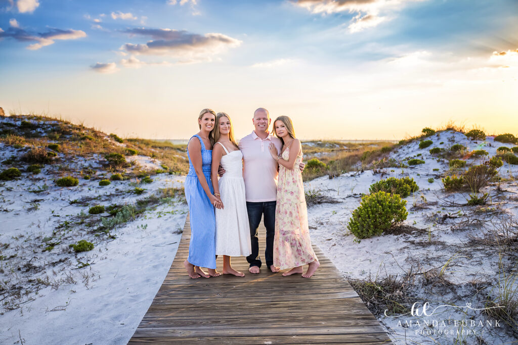 Family of four standing together on the wooden boardwalk at WaterSound Beach at sunset