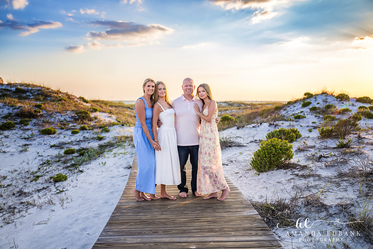 Family of four standing together on the wooden boardwalk at WaterSound Beach at sunset