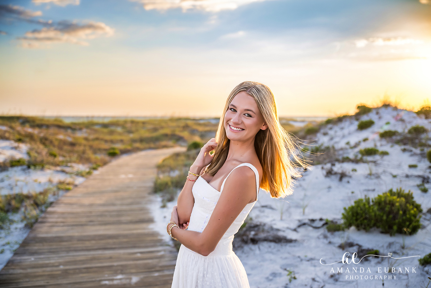 WaterSound Beach Boardwalk Senior Portrait Young woman in a white dress smiling on the boardwalk to WaterSound Beach at sunset