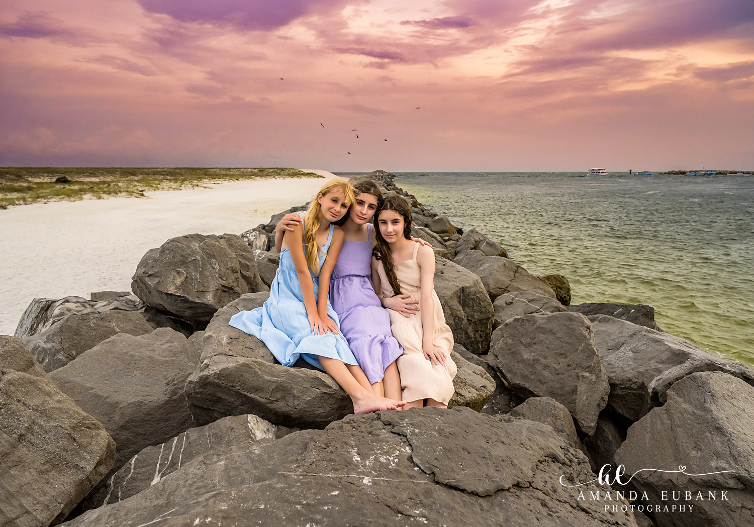Destin Jetties Family Photos | Three girls sitting together Three girls sitting together on the rocks at the Destin Jetties in Destin, Florida at sunset, photographed by Destin family photographer Amanda Eubank